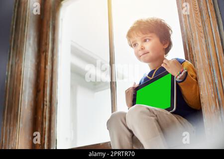 Crescere nell'era digitale: Un ragazzo che usa un tablet mentre si siede su un davanzale. Foto Stock