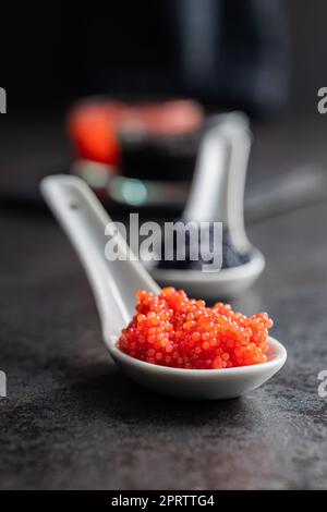 Caviale rosso in cucchiaio di ceramica su tavola scura. Foto Stock