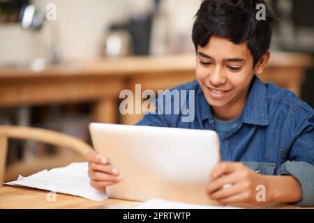 Imparare in digitale. Un giovane adolescente che usa un tablet digitale mentre fa i compiti a casa. Foto Stock