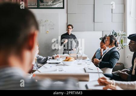 Uomo d'affari con mano sulla anca discutere con i colleghi durante la riunione in ufficio Foto Stock