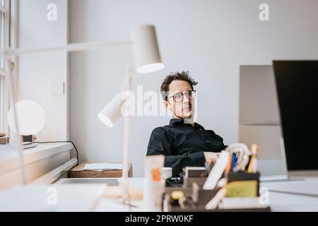 Uomo d'affari che indossa occhiali seduti alla scrivania in ufficio Foto Stock