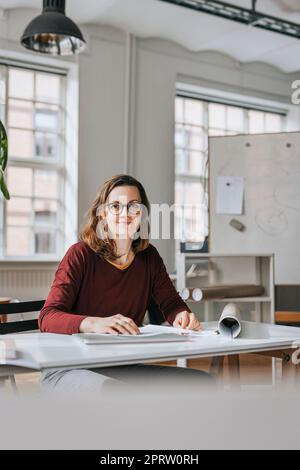 Ritratto di sorridere imprenditrice seduto alla scrivania in ufficio Foto Stock