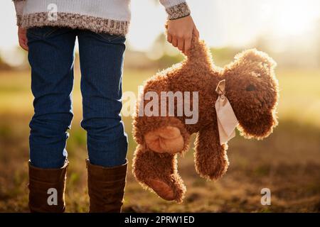 Nessuna infanzia è completa senza un orso preferito. Ripresa da dietro di una bambina non identificabile che cammina nel parco con il suo orsacchiotto Foto Stock