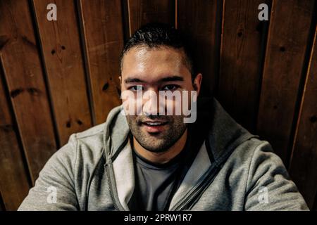 Ritratto di atleta maschile rilassante mentre si siede davanti a una parete di legno Foto Stock