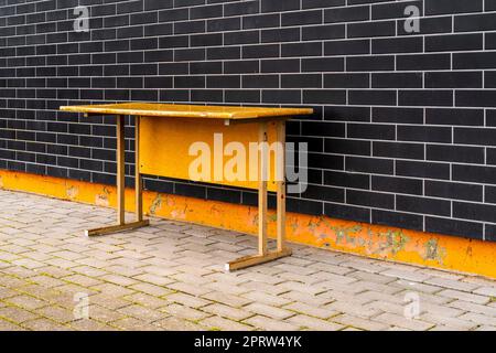 Vecchio banco scuola in legno vicino al muro dell'edificio scolastico Foto Stock