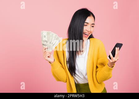 donna shopper sorridente in piedi eccitato tenere in mano il telefono cellulare intelligente online e banconote in dollari Foto Stock