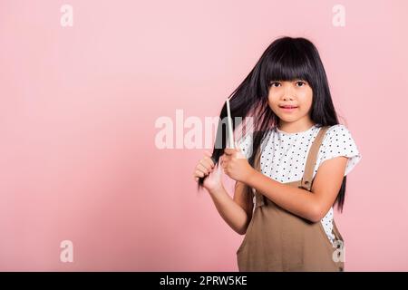 Bambino asiatico 10 anni tenere pettine spazzolarla unruly tocca i suoi lunghi capelli neri Foto Stock