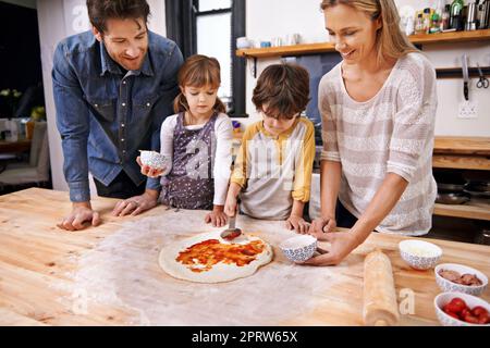 Aggiungere la base di pomodoro... Una pizza fatta in famiglia insieme a casa. Foto Stock