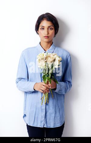 La bellezza perfetta. Studio shot di una giovane donna etnica attraente in possesso di un bouquet di fiori. Foto Stock