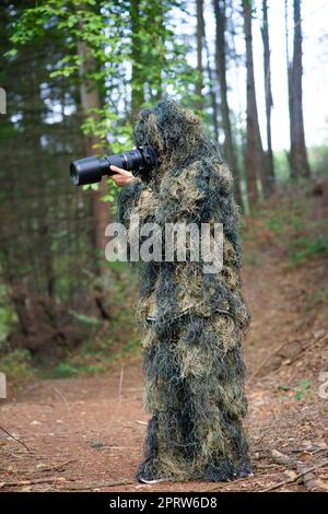 Fotografo che indossa abiti camouflage nella foresta, fotografia di animali selvatici con una macchina fotografica e teleobiettivo Foto Stock