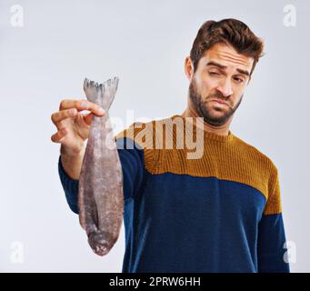 Theres qualcosa di pesce che sta succedendo qui. Studio shot di un uomo che mostra disgusto mentre tiene un pesce puzzolente. Foto Stock