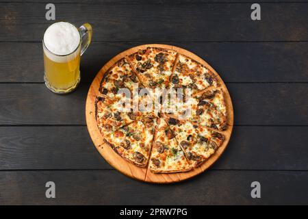 Vista dall'alto della pizza con pasta sottile con funghi e un bicchiere di birra su un tavolo Foto Stock