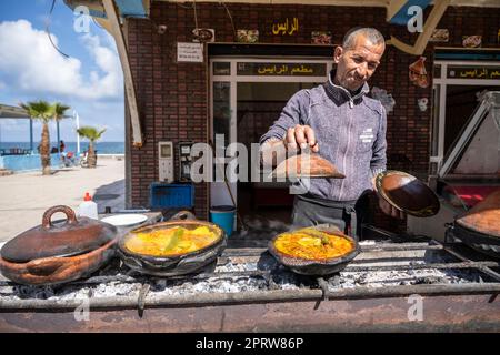 Uomo che cucina la tajine tradizionale in un ristorante di strada nel villaggio di Oued Laou. Foto Stock