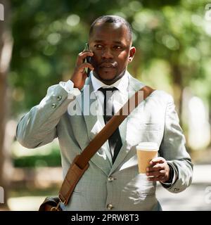 Uomo d'affari africano in strada, ha una telefonata con caffè o tè in tazza. Un uomo nero aziendale ha una conversazione di lavoro al cellulare, camminando per fare una pausa pranzo in città o in città Foto Stock