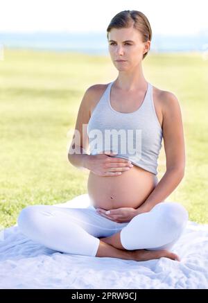 Rimanere in forma di punta superiore durante la sua gravidanza. Una bella donna incinta che fa yoga all'aperto. Foto Stock