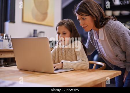 Navigare in internet con la supervisione di mommys. Una giovane ragazza che studia con la madre nelle vicinanze per aiutare. Foto Stock