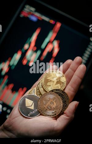 Mano che tiene varie monete di criptovaluta d'oro con grafico a bastone di candela e sfondo digitale. Bitcoin, Ethereum, Litecoin, Dogecoin. Foto Stock