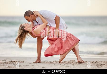 L'amore, la danza e la danza di coppia in spiaggia in estate celebrano il loro matrimonio, la felicità e la luna di miele. Sorriso, tramonto e donna felice che festeggia un sano rapporto con il partner in mare Foto Stock