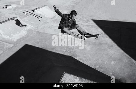 HES ha abilità. Uno scatto in bianco e nero di uno skateboarder che fa trucchi in uno skatepark. Foto Stock