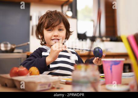 Dipingi ardentemente il mio uovo di pasqua. Ritratto di un ragazzino che dipinge un uovo blu. Foto Stock