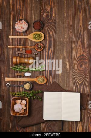 Vista dall'alto del ricettario aperto per ricette posizionate accanto a cucchiai da cucina e ciotole con spezie e condimenti Foto Stock