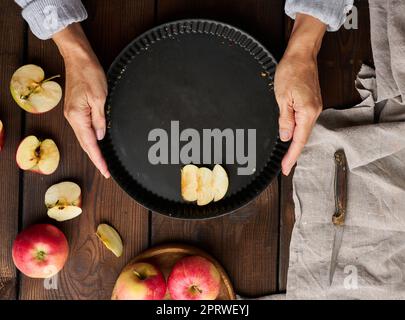 Una donna mette le fette di mela in una teglia rotonda sul tavolo, accanto agli ingredienti. Vista dall'alto Foto Stock