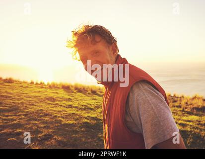 Amare il tempo lontano dalla città. Ritratto di un uomo in piedi su una collina al tramonto con l'oceano sullo sfondo. Foto Stock