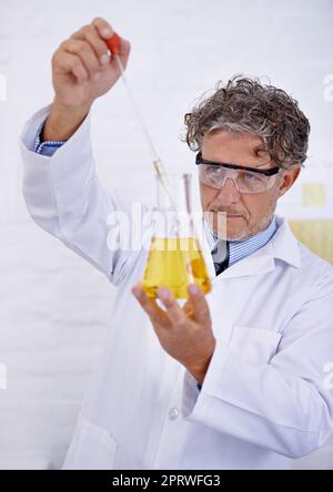 Condurre con attenzione il suo esperimento. Un colpo corto di uno scienziato maturo che gocciola liquido in una fiasca nel suo laboratorio. Foto Stock