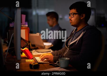 Un gruppo di giovani colleghi che lavorano in un ufficio poco illuminato. Foto Stock