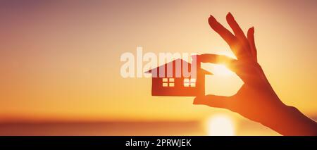 Mano di donna che tiene un modello di una casa la sera del tramonto Foto Stock