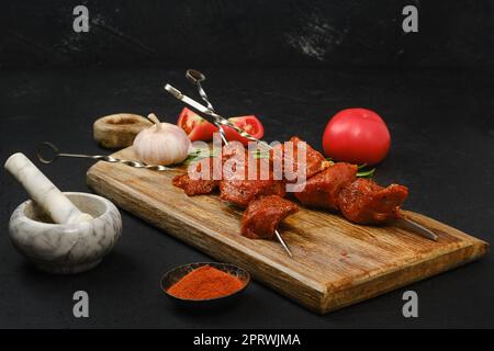 Spiedini con carne di maiale cruda marinata su sfondo scuro Foto Stock