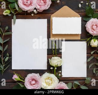 Cartoline e busta tra rose rosa e crema con vista dall'alto in legno marrone, mockup nuziale Foto Stock