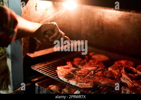 Il gusto del cibo alla griglia è così unico. Primo piano di un uomo irriconoscibile grigliare carne mentre si fa un barbecue. Foto Stock