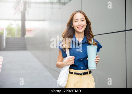 donna d'affari sicura sorridente con sacchetto di stoffa che tiene thermos thermos di acciaio tumbler tazza vetro d'acqua Foto Stock