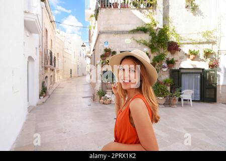 Bella giovane donna gioiosa che sorride e guarda la macchina fotografica. Ritratto di una giovane donna abbronzata con cappello e abito arancione che si gode le vacanze estive in Italia. Foto Stock