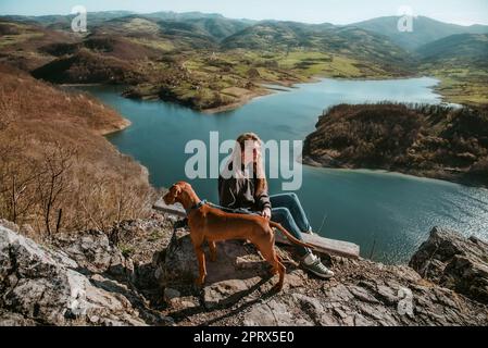 Donna e cane sulla cima della montagna sopra il fiume Foto Stock