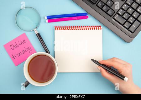 top view online training scritto su sticky note tazza di tea marker in femmina mano tastiera lupa notepad marker su sfondo blu Foto Stock