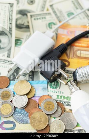 Il concetto di crisi energetica, gli aumenti di prezzo. Banconote in euro e dollari, monete sullo sfondo di una lampada, spina, cavo. Tempo fiscale, pagamento fattura, c Foto Stock