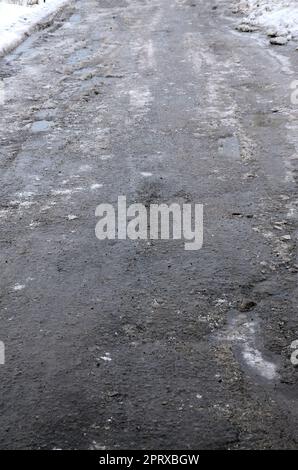Strada asfaltata danneggiata con buche causate da cicli di congelamento e scongelamento durante l'inverno. Strada povera Foto Stock