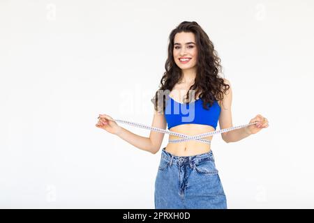 Donna che misura la vita e mostra quanto peso ha perso in jeans, su uno sfondo bianco. Foto Stock