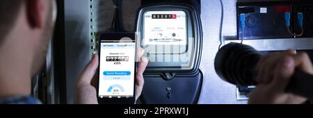 Elettricista che legge il contatore di energia usando il telefono mobile Foto Stock