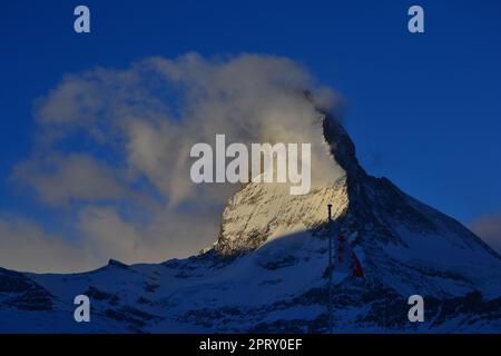 Il Cervino con nuvole mistiche e cielo blu con una bandiera di wallis di fronte Foto Stock