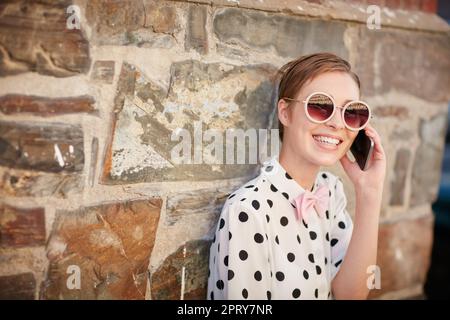 I suoi amici sanno come raggiungerla. Ritratto di una giovane donna alla moda che usa il telefono mentre si appoggia a una parete esterna Foto Stock