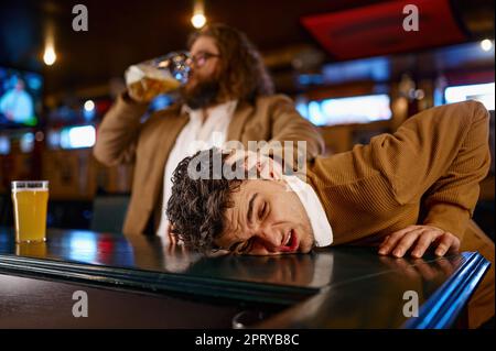 Comportamento pazzo dei tifosi di calcio al pub sportivo. Uomo che tira la faccia di un altro ragazzo sul banco del bar e beve birra Foto Stock