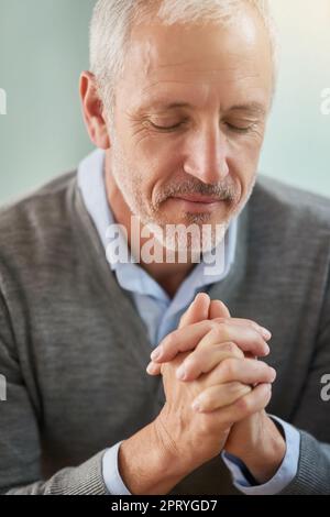 Cercare una guida dall'alto. un uomo d'affari maturo che prega mentre si siede nel suo ufficio Foto Stock