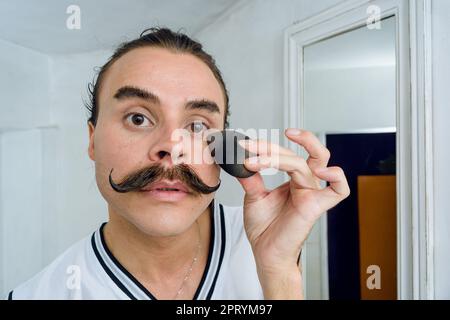 ritratto di giovane latina di etnia argentina sesso non-binaria persona nella sua stanza, lei è seria guardando la fotocamera mentre applicando trucco wit Foto Stock