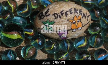 Una pietra con essere diverso scritto su di essa. Tre uccelli su una corda con una consegna verso il basso. Circondato da mumbles colorati. Foto Stock