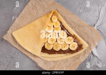 Crepes ripiene di cioccolato da spalmare e banana sulla piastra bianca. Frittelle sottili, blini. Dolce con. Foto Stock