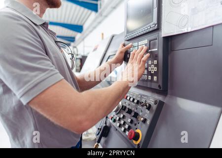 Operatore di produzione che programma macchine utensili CNC industriali mentre immette i dati di lavoro Foto Stock