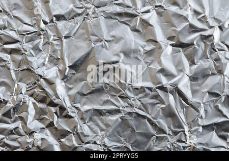 Sottile foglio stropicciato di alluminio stagnato argento sfondo con superficie lucida stropicciata per la texture Foto Stock